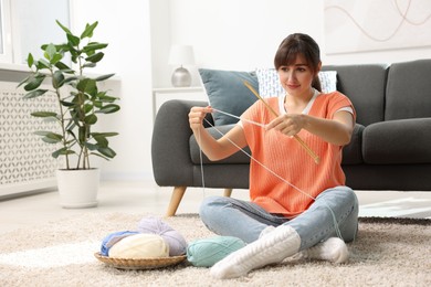 Photo of Beautiful woman knitting with needles on floor at home