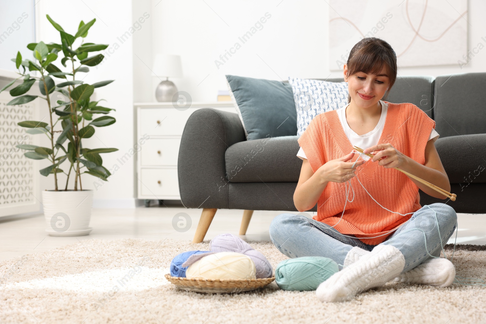 Photo of Beautiful woman knitting with needles on floor at home