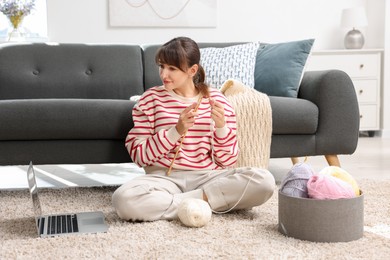 Photo of Beautiful woman learning to knit with online course on floor at home