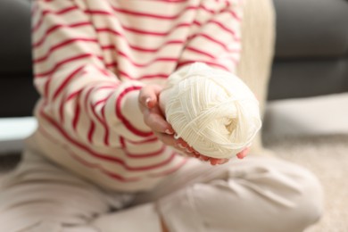 Photo of Woman with yarn on floor at home, closeup. Knitting material