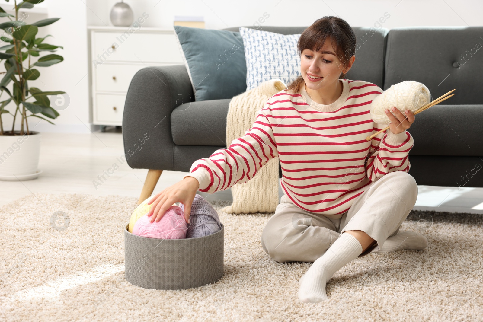 Photo of Beautiful woman with colorful yarns and knitting needles on floor at home