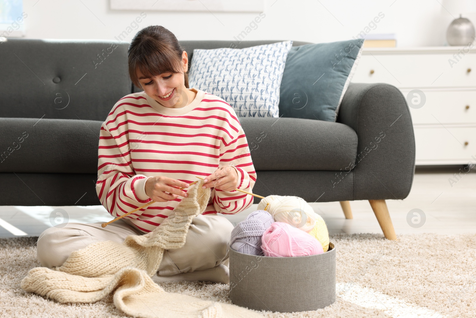 Photo of Beautiful woman knitting with needles on floor at home