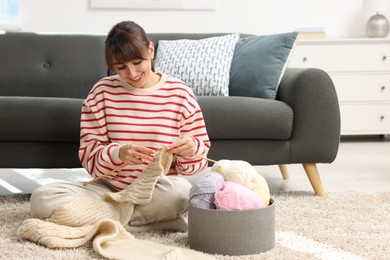 Beautiful woman knitting with needles on floor at home