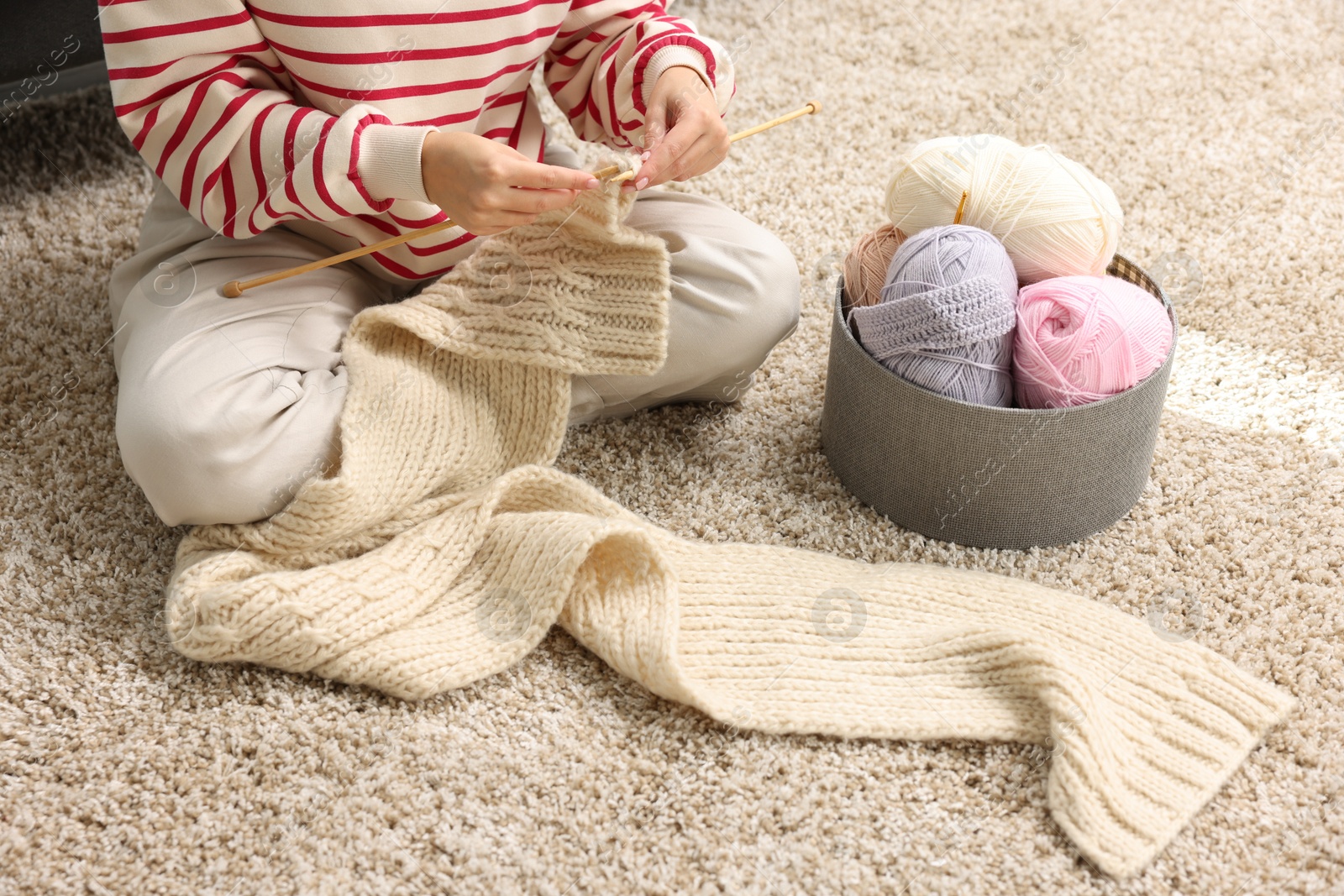 Photo of Woman knitting with needles on floor at home, closeup