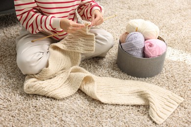 Photo of Woman knitting with needles on floor at home, closeup