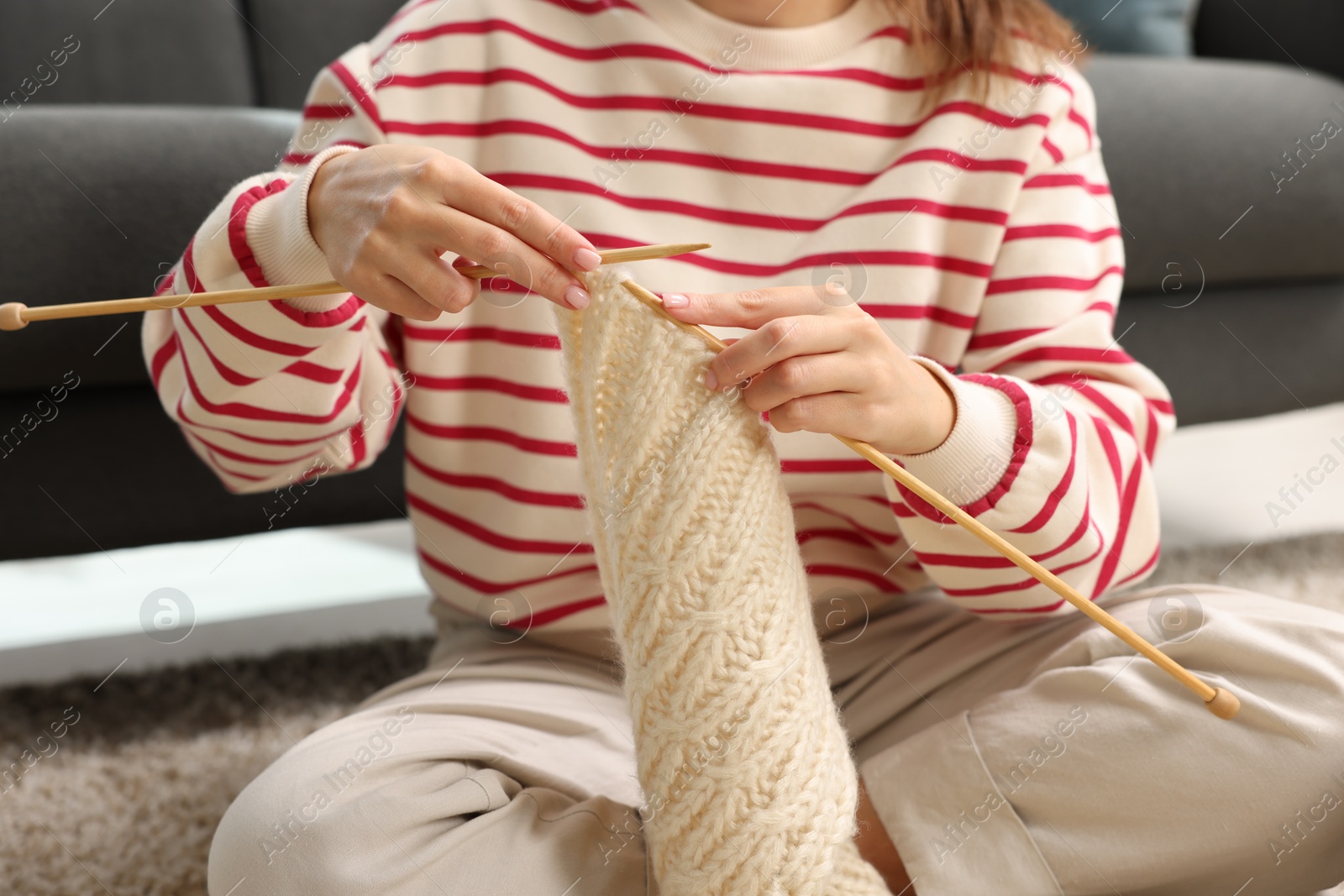 Photo of Woman knitting with needles on floor at home, closeup