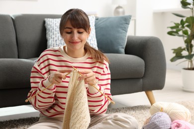 Beautiful woman knitting with needles on floor at home