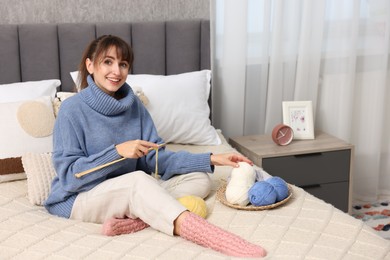 Beautiful woman knitting with needles on bed at home