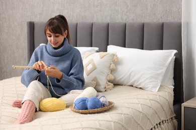 Beautiful woman knitting with needles on bed at home