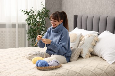 Photo of Beautiful woman knitting with needles on bed at home