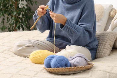 Woman knitting with needles on bed at home, closeup