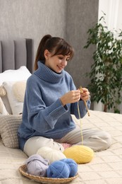 Beautiful woman knitting with needles on bed at home