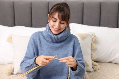 Beautiful woman knitting with needles on bed at home