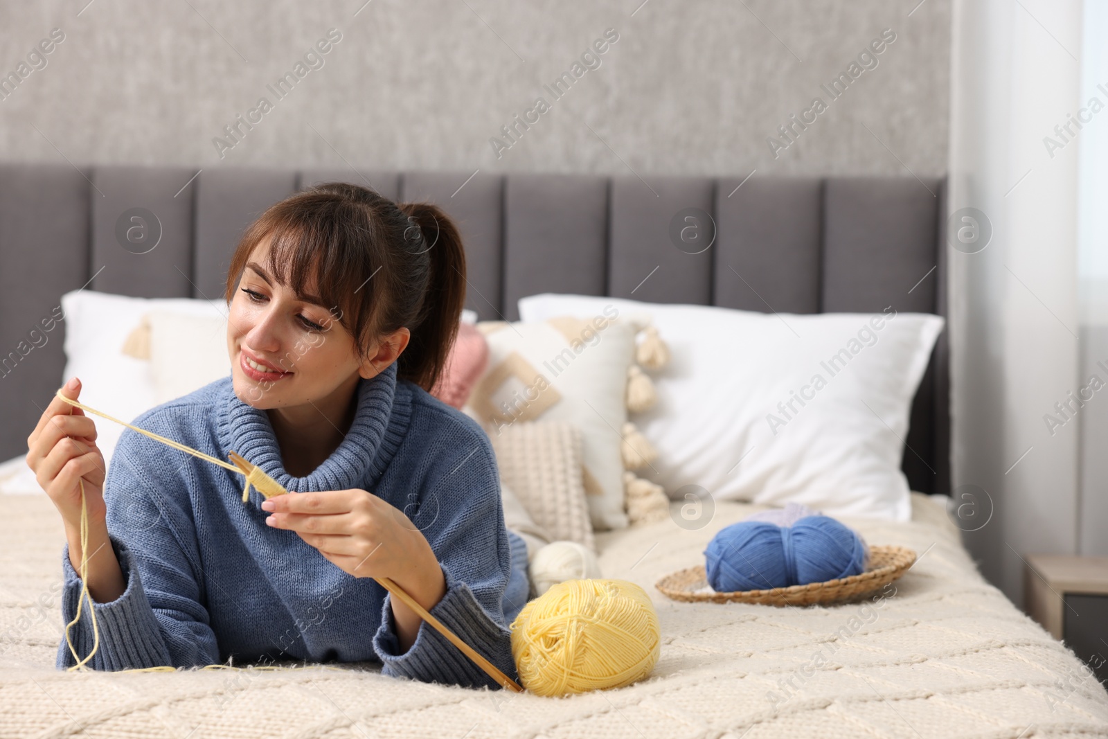 Photo of Beautiful woman knitting with needles on bed at home