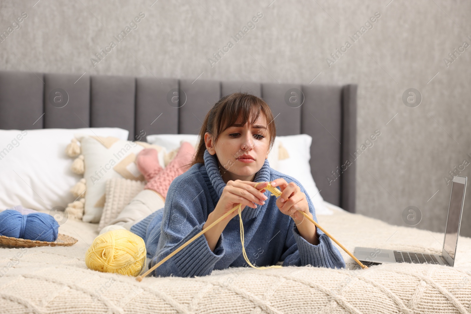 Photo of Woman learning to knit with online course on bed at home