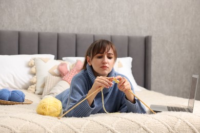 Woman learning to knit with online course on bed at home