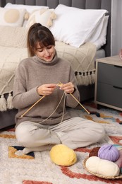 Photo of Beautiful woman knitting with needles on floor at home