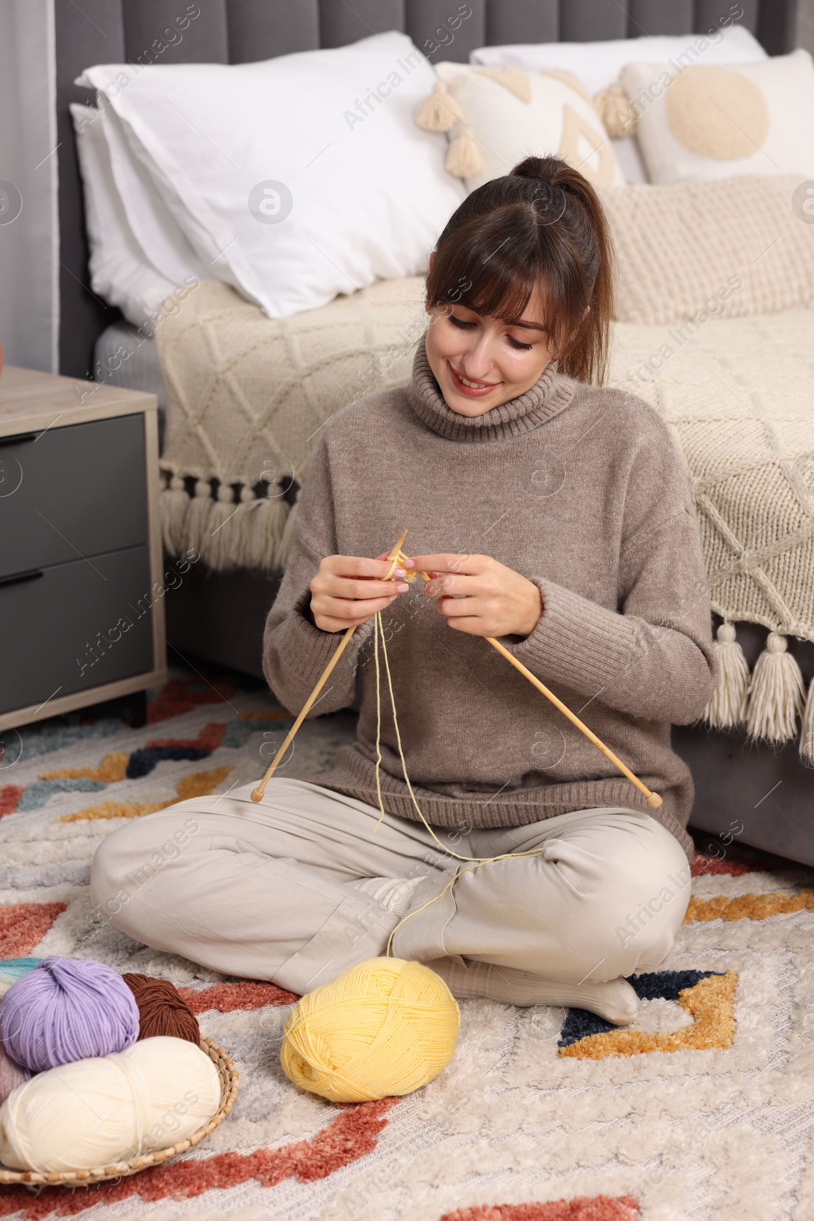 Photo of Beautiful woman knitting with needles on floor at home