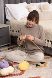 Beautiful woman knitting with needles on floor at home