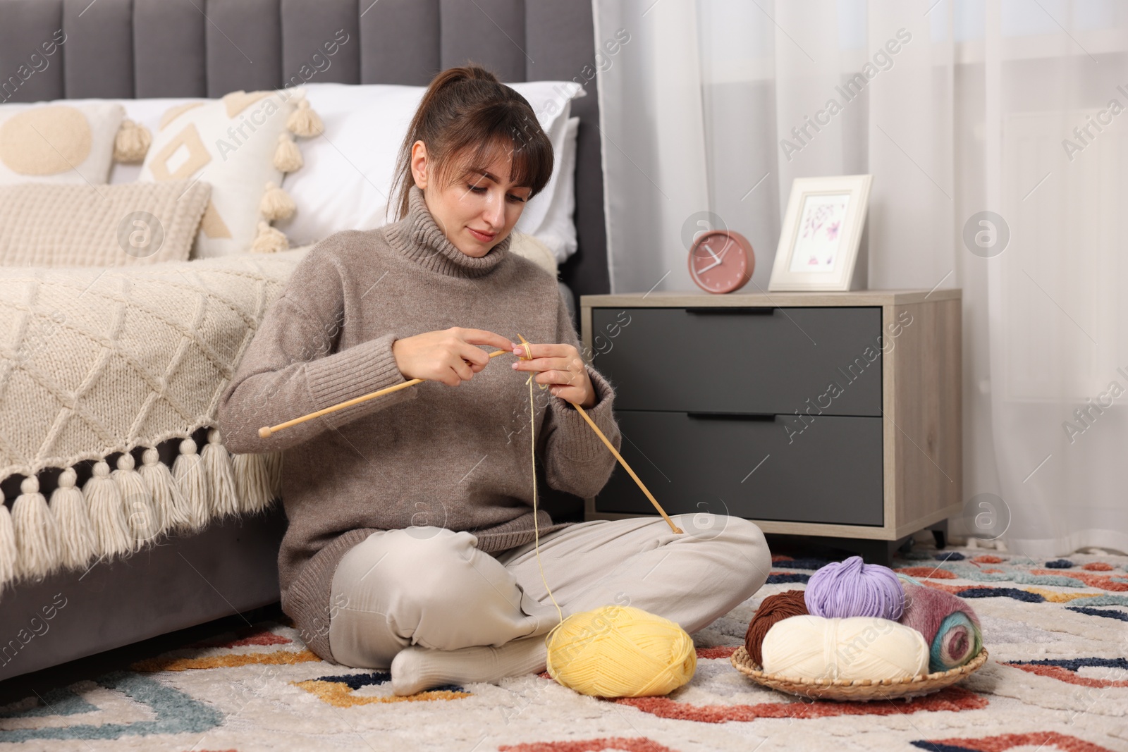 Photo of Beautiful woman knitting with needles on floor at home