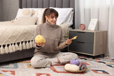 Photo of Beautiful woman with colorful yarns and knitting needles on floor at home