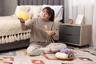 Beautiful woman with colorful yarns and knitting needles on floor at home