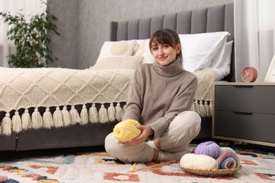 Beautiful woman with colorful yarns and knitting needles on floor at home