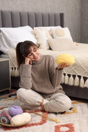 Beautiful woman with colorful yarns and knitting needles on floor at home