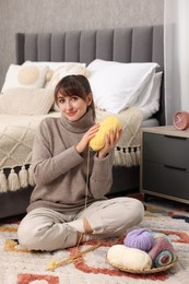 Beautiful woman with colorful yarns and knitting needles on floor at home