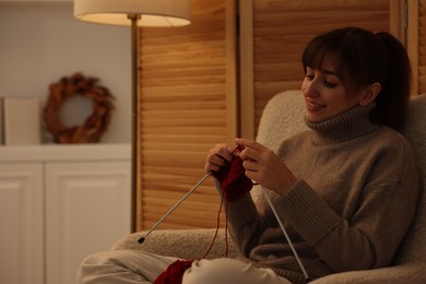 Photo of Beautiful woman knitting with needles in armchair at home