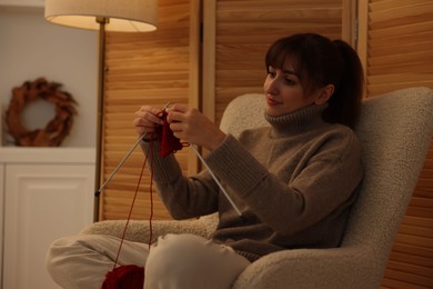 Beautiful woman knitting with needles in armchair at home