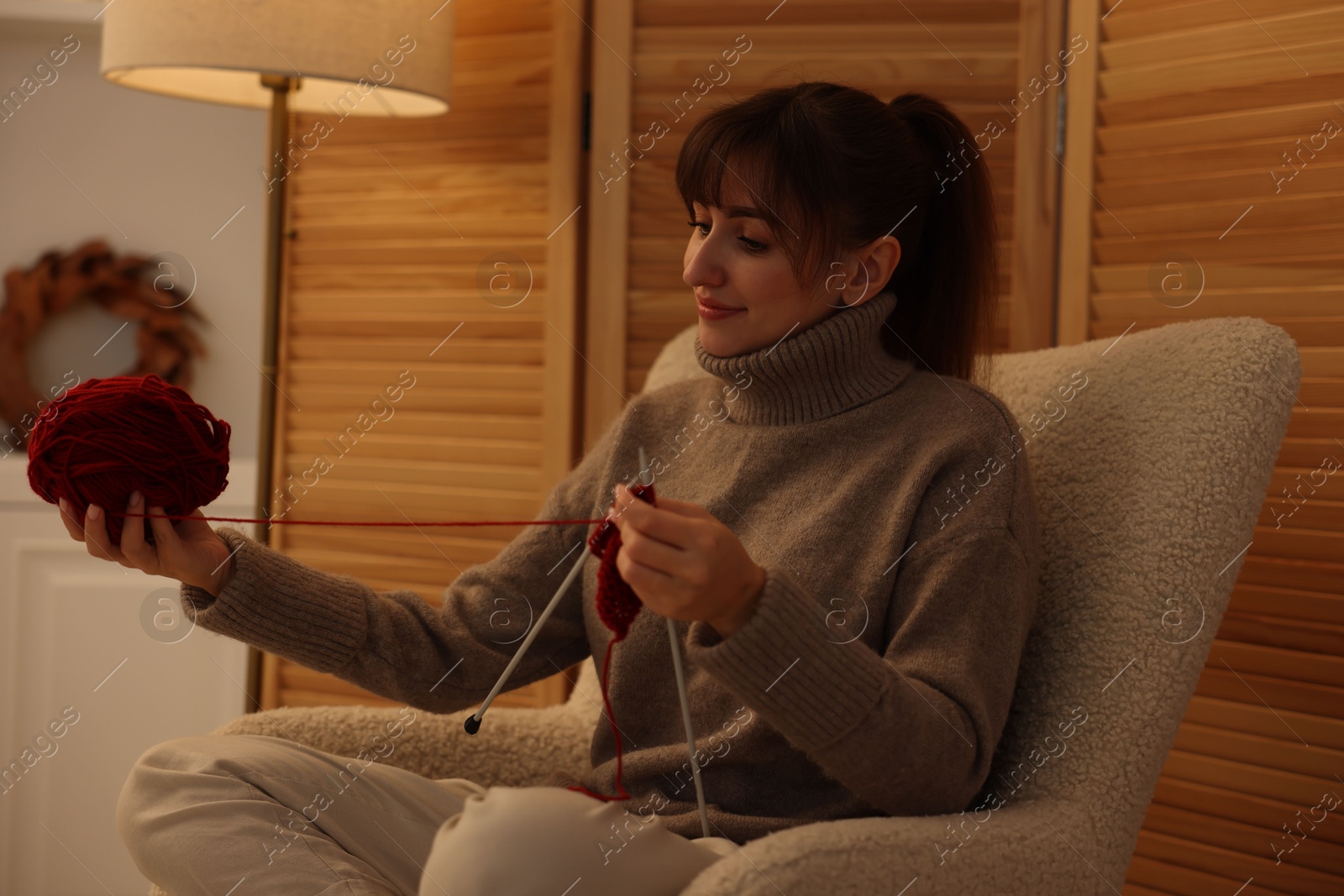 Photo of Beautiful woman knitting with needles in armchair at home