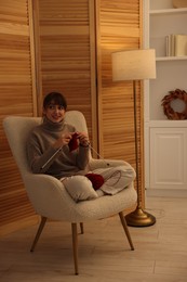 Photo of Beautiful woman knitting with needles in armchair at home