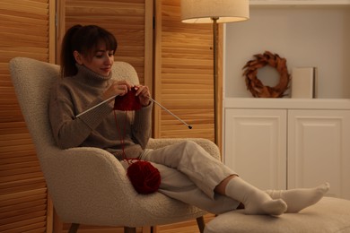 Beautiful woman knitting with needles in armchair at home