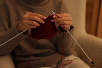 Photo of Woman knitting with needles in armchair at home, closeup