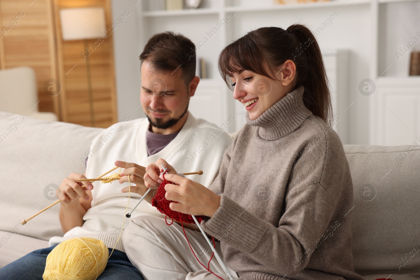 Photo of Woman teaching her boyfriend how to knit on sofa at home