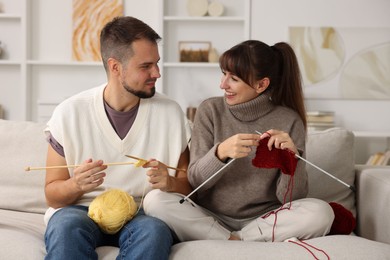 Photo of Woman teaching her boyfriend how to knit on sofa at home