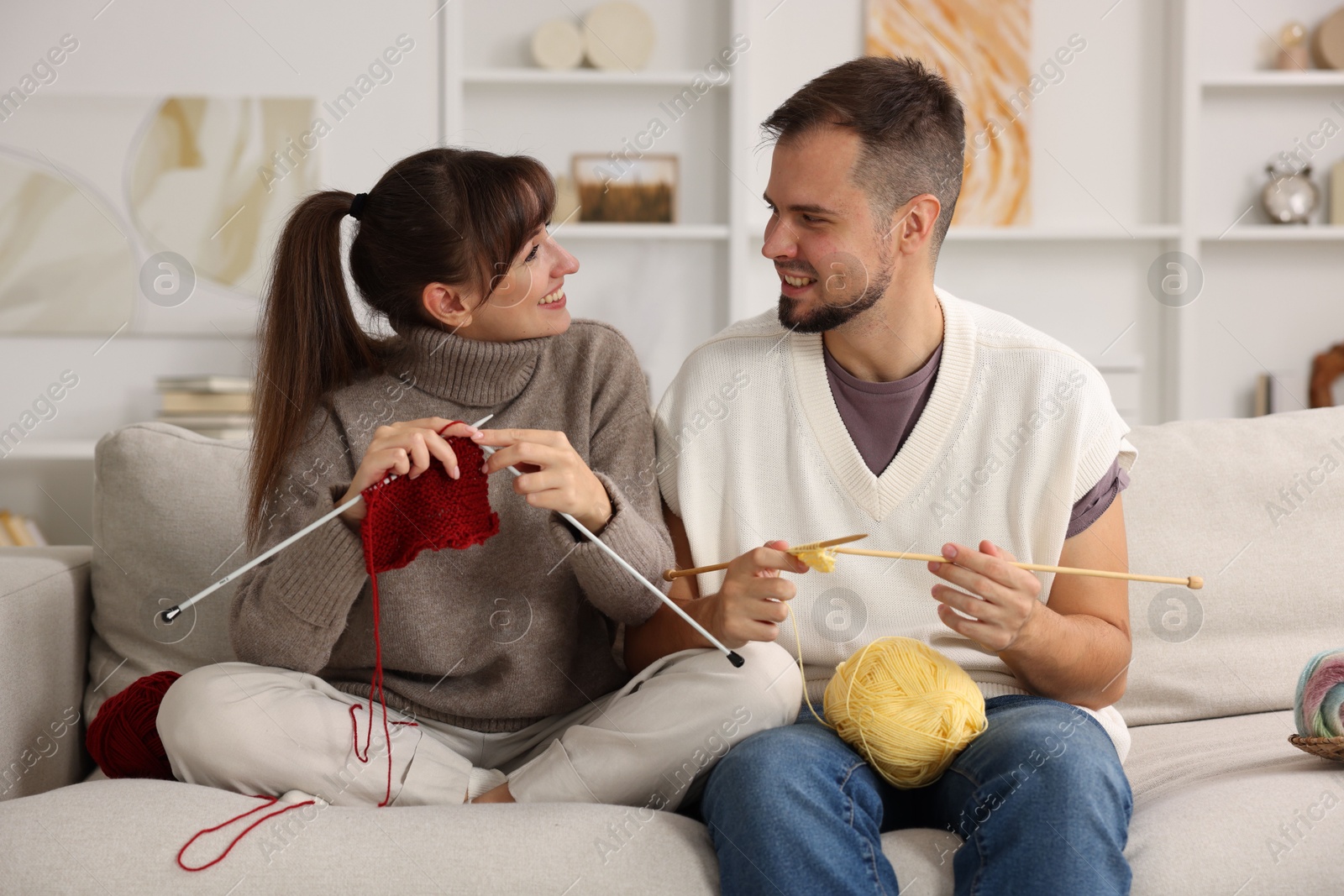 Photo of Woman teaching her boyfriend how to knit on sofa at home