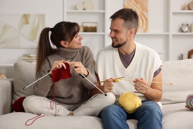 Photo of Woman teaching her boyfriend how to knit on sofa at home