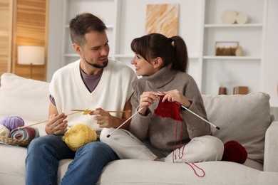 Photo of Woman teaching her boyfriend how to knit on sofa at home