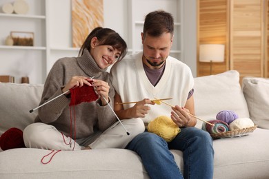 Woman teaching her boyfriend how to knit on sofa at home