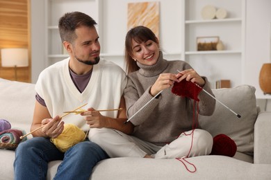 Woman teaching her boyfriend how to knit on sofa at home