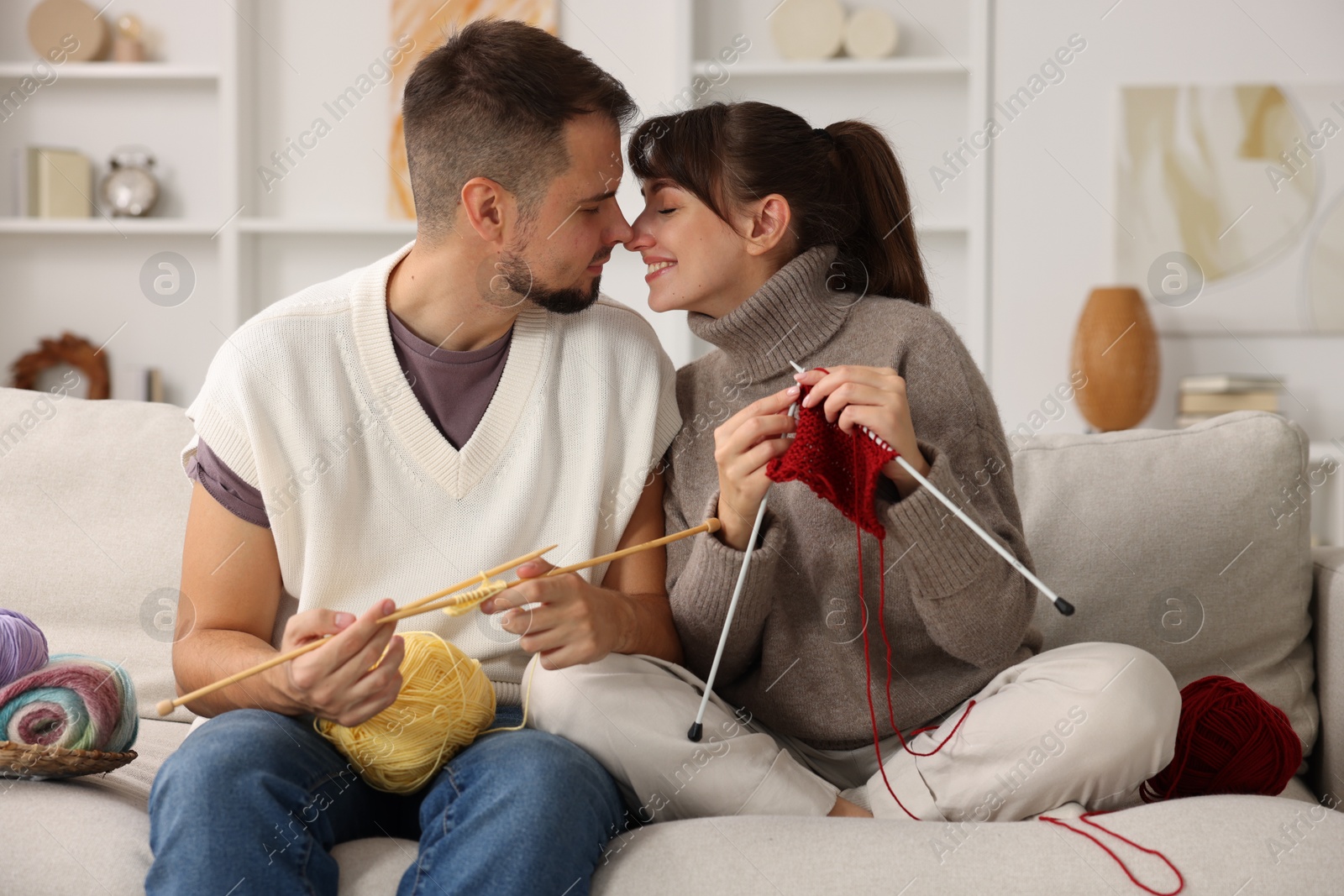 Photo of Woman teaching her boyfriend how to knit on sofa at home