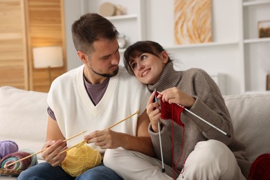 Photo of Woman teaching her boyfriend how to knit on sofa at home