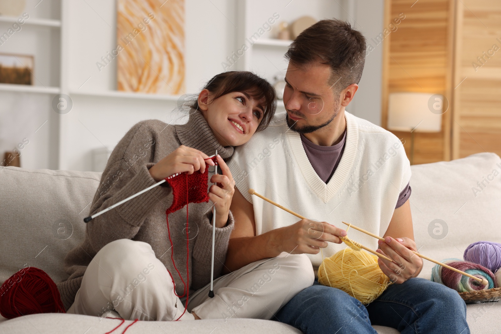 Photo of Woman teaching her boyfriend how to knit on sofa at home