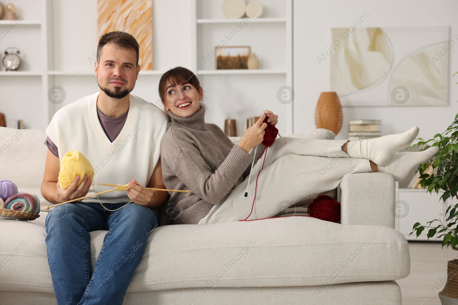 Photo of Woman teaching her boyfriend how to knit on sofa at home