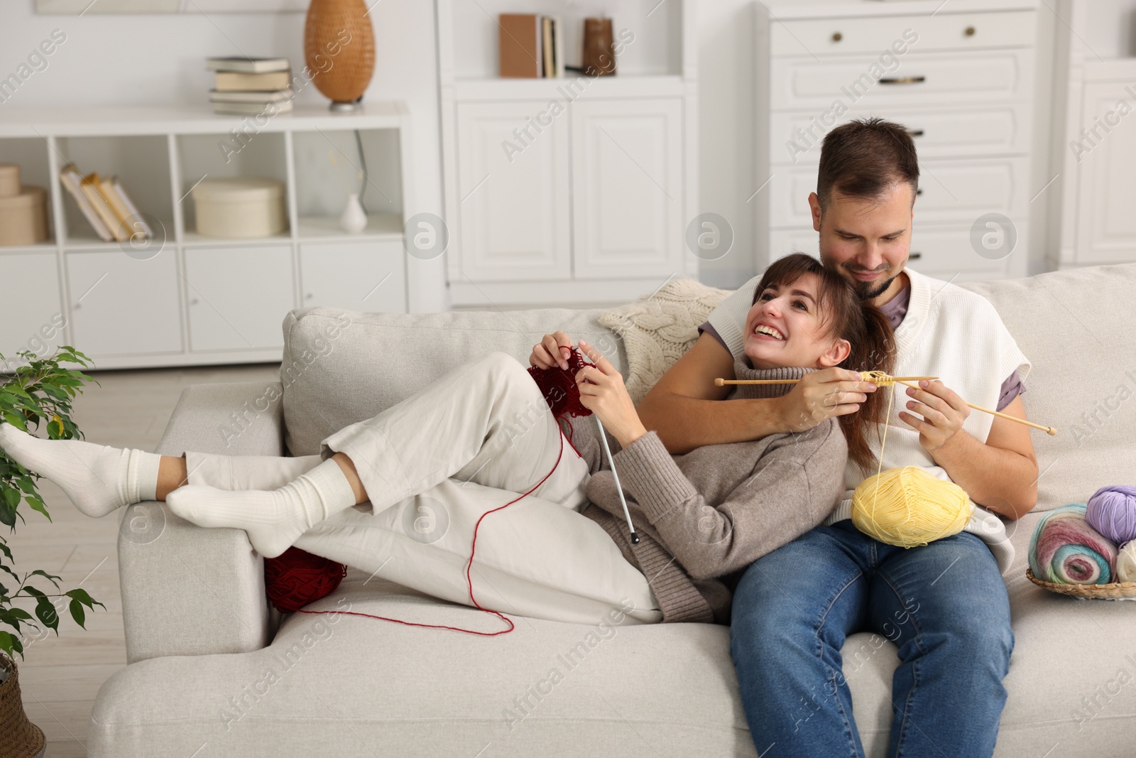 Photo of Woman teaching her boyfriend how to knit on sofa at home