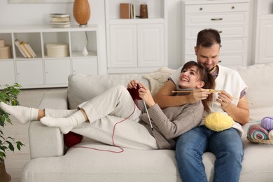 Woman teaching her boyfriend how to knit on sofa at home