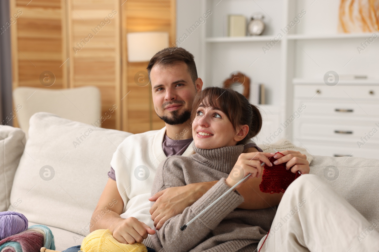 Photo of Woman teaching her boyfriend how to knit on sofa at home