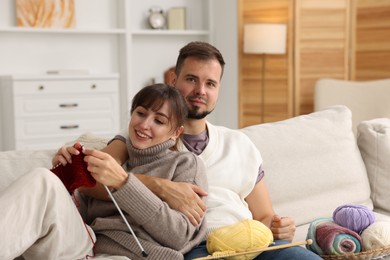 Woman teaching her boyfriend how to knit on sofa at home